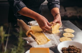 Person formt Teigtaschen auf bemehlter Arbeitsfläche.