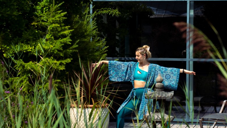 Eine Frau in blauer Yogakleidung macht eine Yoga-Pose im Freien neben einem Teich und Pflanzen.