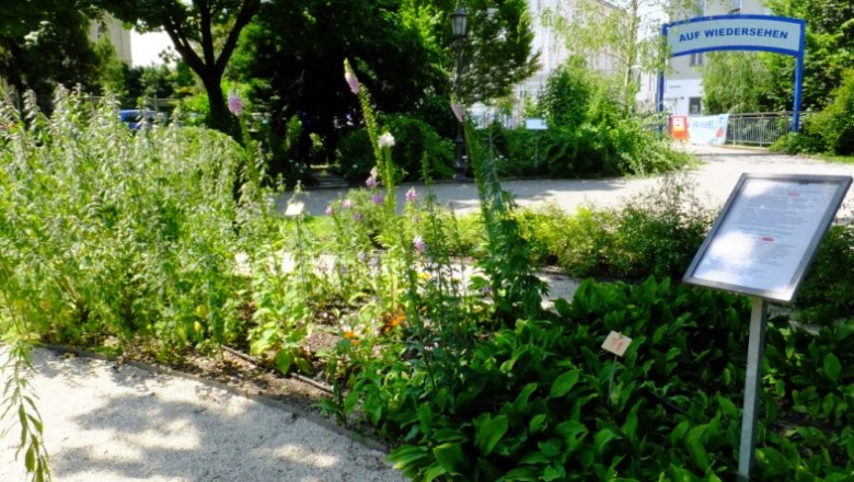 Ein gepflegter Garten mit Pflanzen und einem Schild, im Hintergrund ein Tor mit der Aufschrift 'Auf Wiedersehen'.