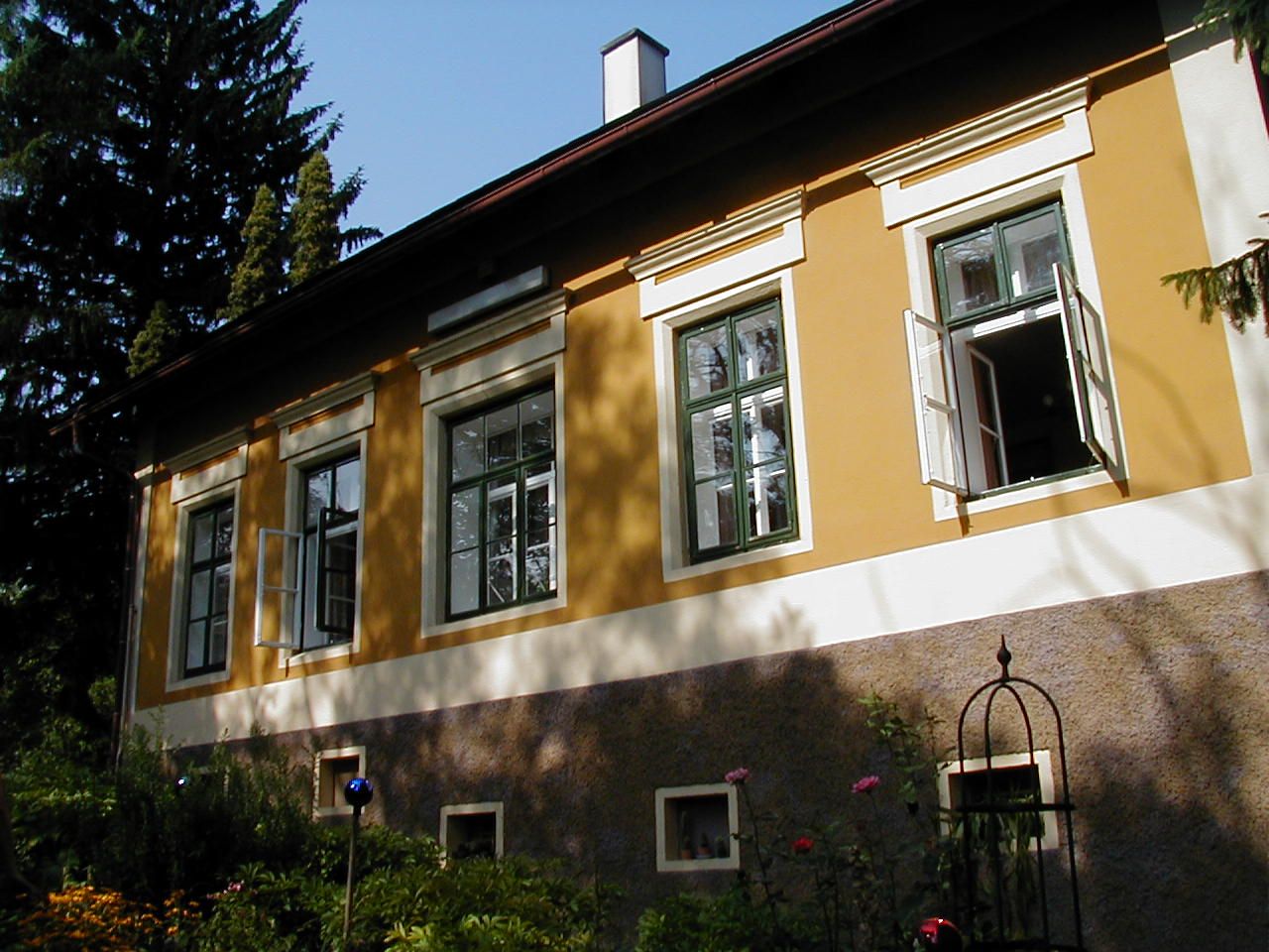 Gelbes Haus mit offenen Fenstern und Garten im Vordergrund.