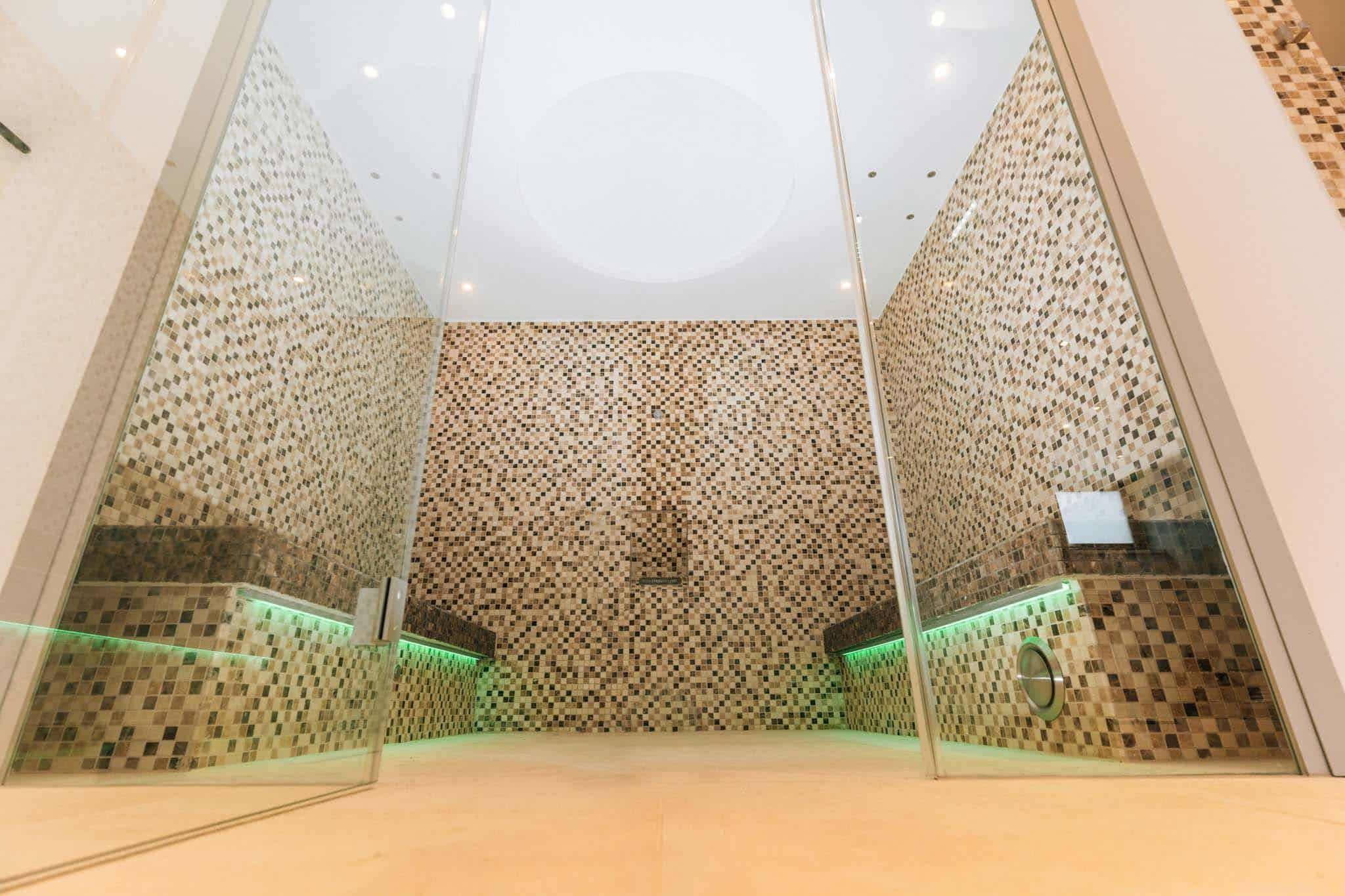 Innenansicht einer modernen Sauna mit Mosaikfliesen und Glaswänden.