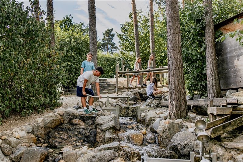 Kinder spielen an einem Wasserlauf in einem Erlebnisgarten.