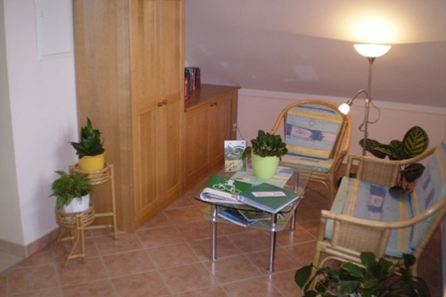 Gemütliche Leseecke mit Rattanmöbeln, Pflanzen und einem kleinen Tisch mit Büchern.