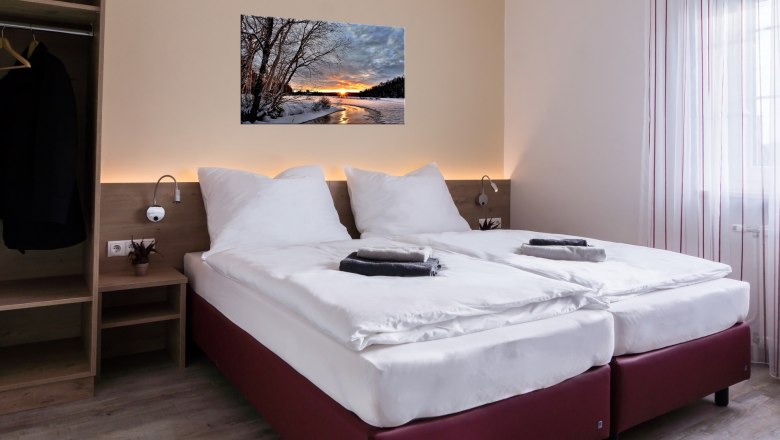 Modernes Doppelzimmer mit zwei Einzelbetten, Bild an der Wand, Kleiderschrank und Fenster mit Vorh&auml;ngen.