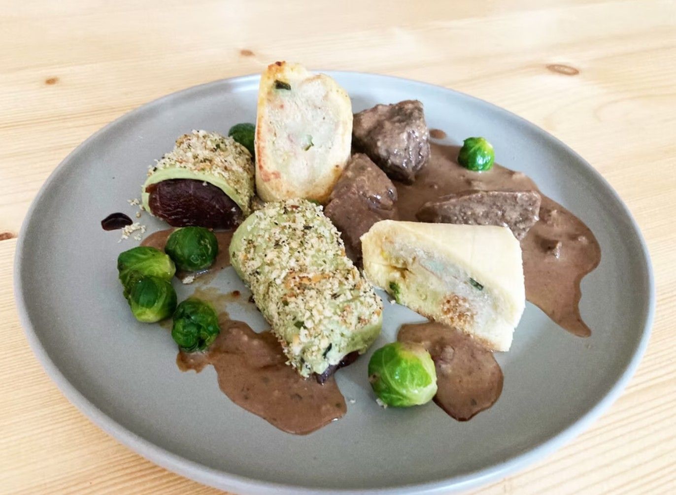 Ein Teller mit Fleisch, Rosenkohl und gefüllten Teigrollen auf einer braunen Sauce.