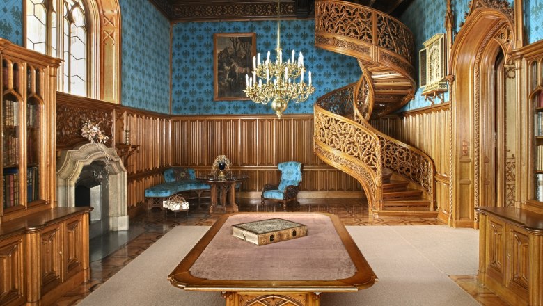 Innenansicht eines pr&auml;chtigen Raumes im Schloss Lednice mit einer kunstvoll geschnitzten Wendeltreppe und einem gro&szlig;en Tisch in der Mitte.