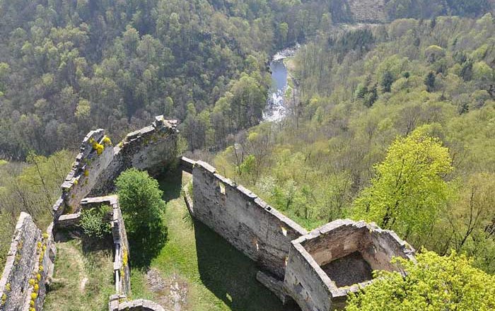 Ruinen einer alten Burg mit Blick auf bewaldete H&uuml;gel und einen Fluss im Hintergrund.