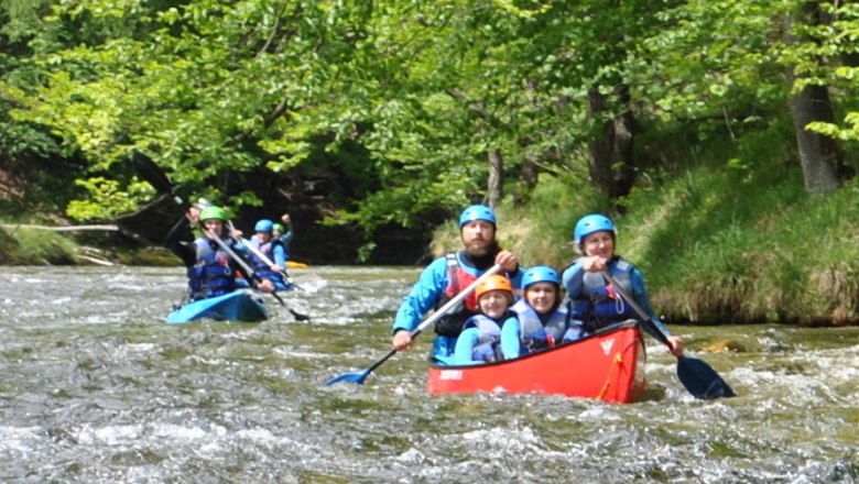 Menschen in Kanus paddeln auf einem Fluss in einer grünen Waldlandschaft.