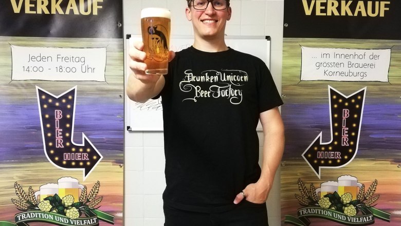 Person h&auml;lt ein Bierglas vor zwei Bannern mit der Aufschrift 'Ab Hof Verkauf'.
