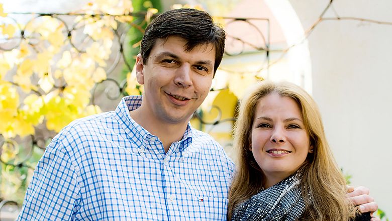 Ein Mann und eine Frau lächeln in die Kamera, im Hintergrund herbstliche Blätter.