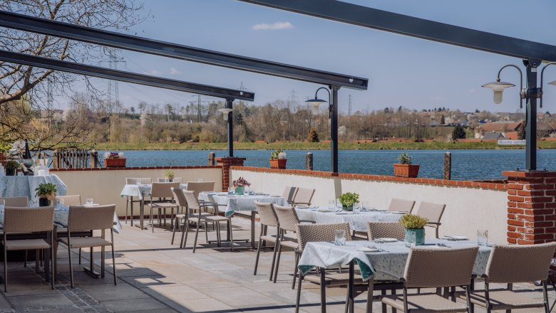 Terrasse mit Tischen und Stühlen, Blick auf einen Stausee und umliegende Landschaft.