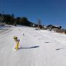Skifahrer auf einer sonnigen Piste in M&ouml;nichkirchen mit Sessellift und Schneekanonen.