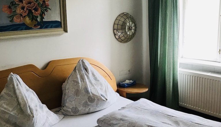 Ein gem&uuml;tliches Schlafzimmer mit Doppelbett, gr&uuml;nen Vorh&auml;ngen und einem Blumenbild an der Wand.