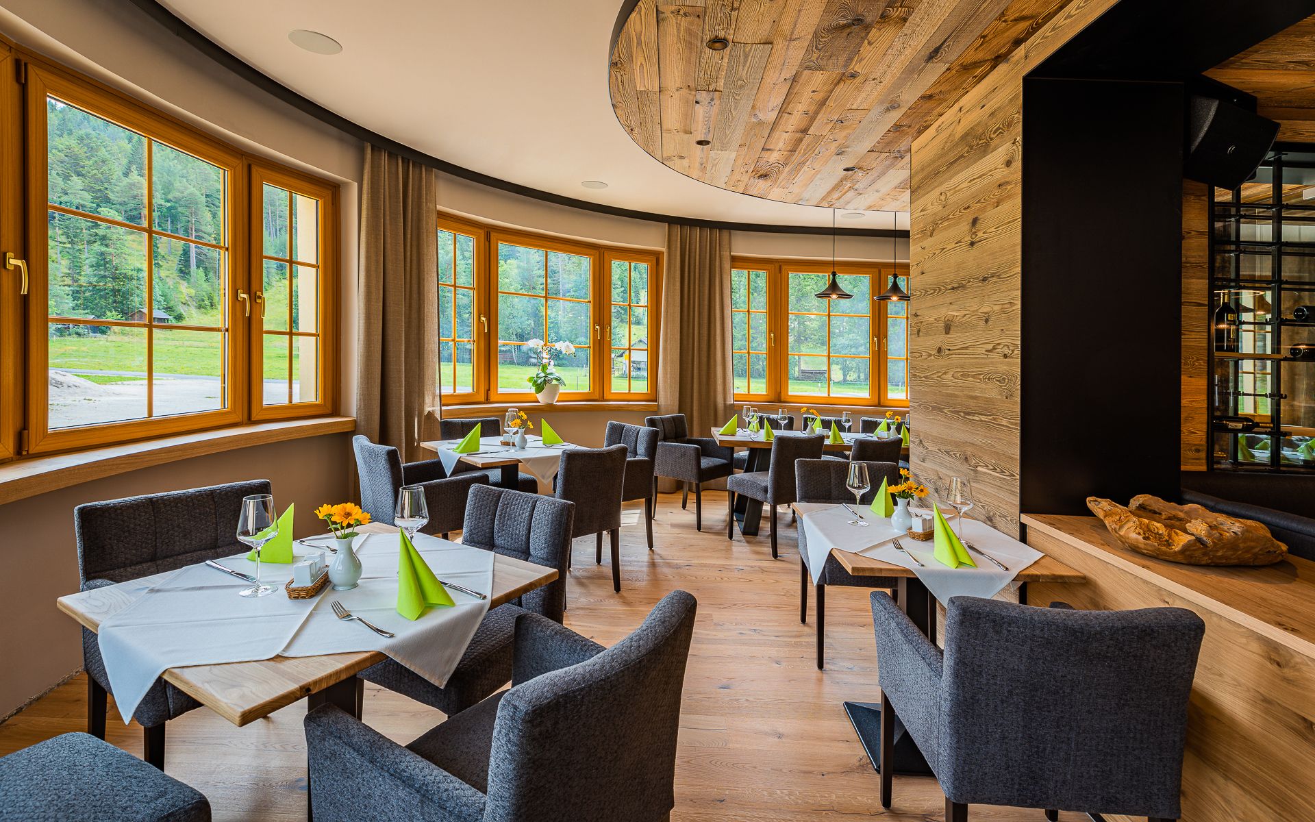 Elegantes Restaurant mit Holzelementen, gedeckten Tischen und großen Fenstern mit Blick ins Grüne.