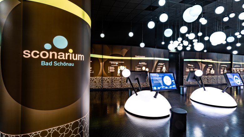 Innenansicht der Ausstellung Sconarium in Bad Schönau mit interaktiven Displays und leuchtenden Kugeln an der Decke.