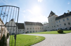 Eingang von Schloss Walpersdorf mit offenem Tor, Rasenfl&auml;che und historischem Geb&auml;ude im Hintergrund.