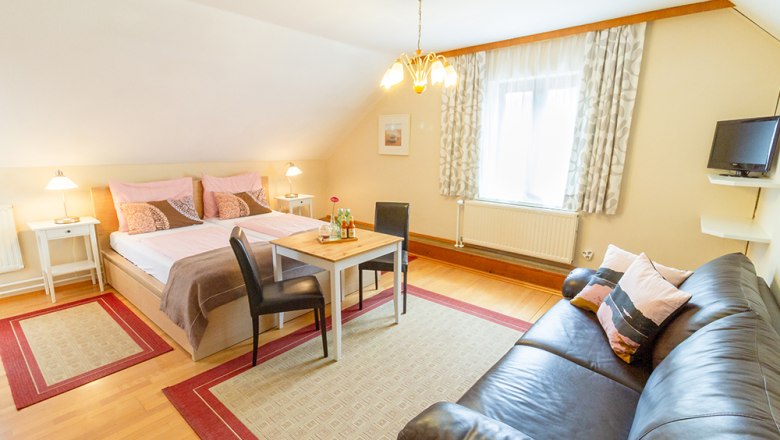 Gem&uuml;tliches G&auml;stezimmer mit Doppelbett, Sofa, Tisch und St&uuml;hlen, helle Einrichtung.