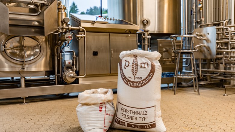 Säcke mit Gerstenmalz in einer Brauerei vor Edelstahlmaschinen.