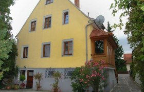Gelbes Gästehaus mit Holzveranda und blühenden Pflanzen.