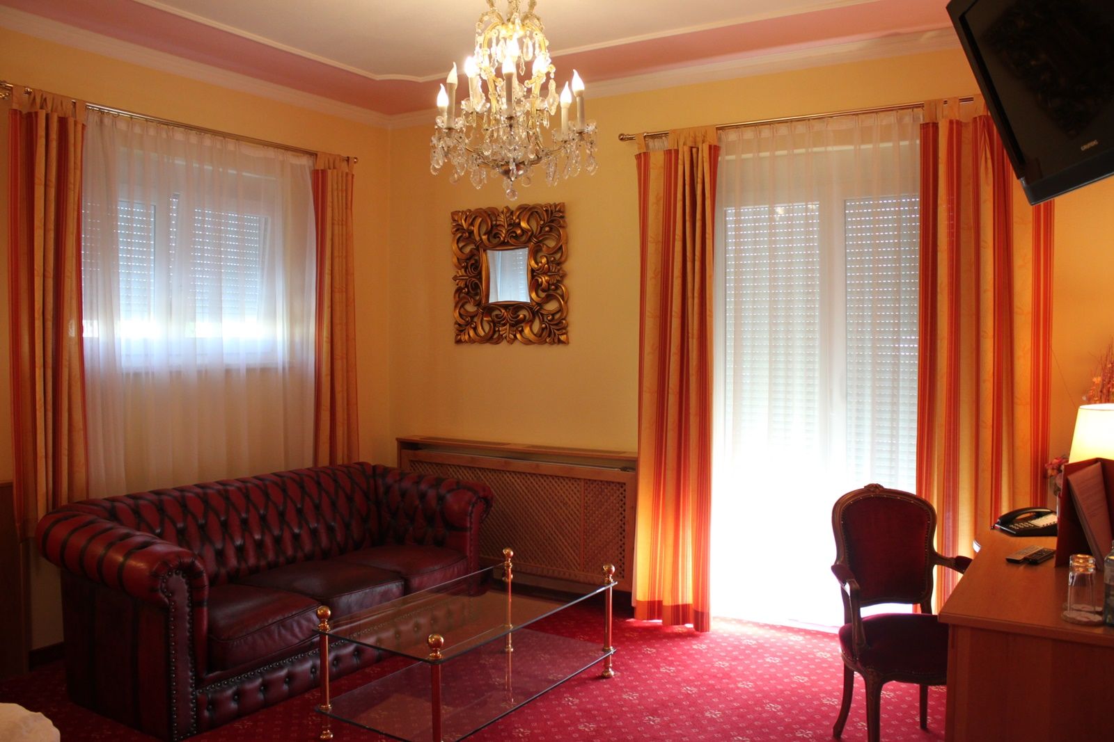 Elegantes Wohnzimmer mit Ledersofa, Glastisch, Kronleuchter und roten Vorhängen.