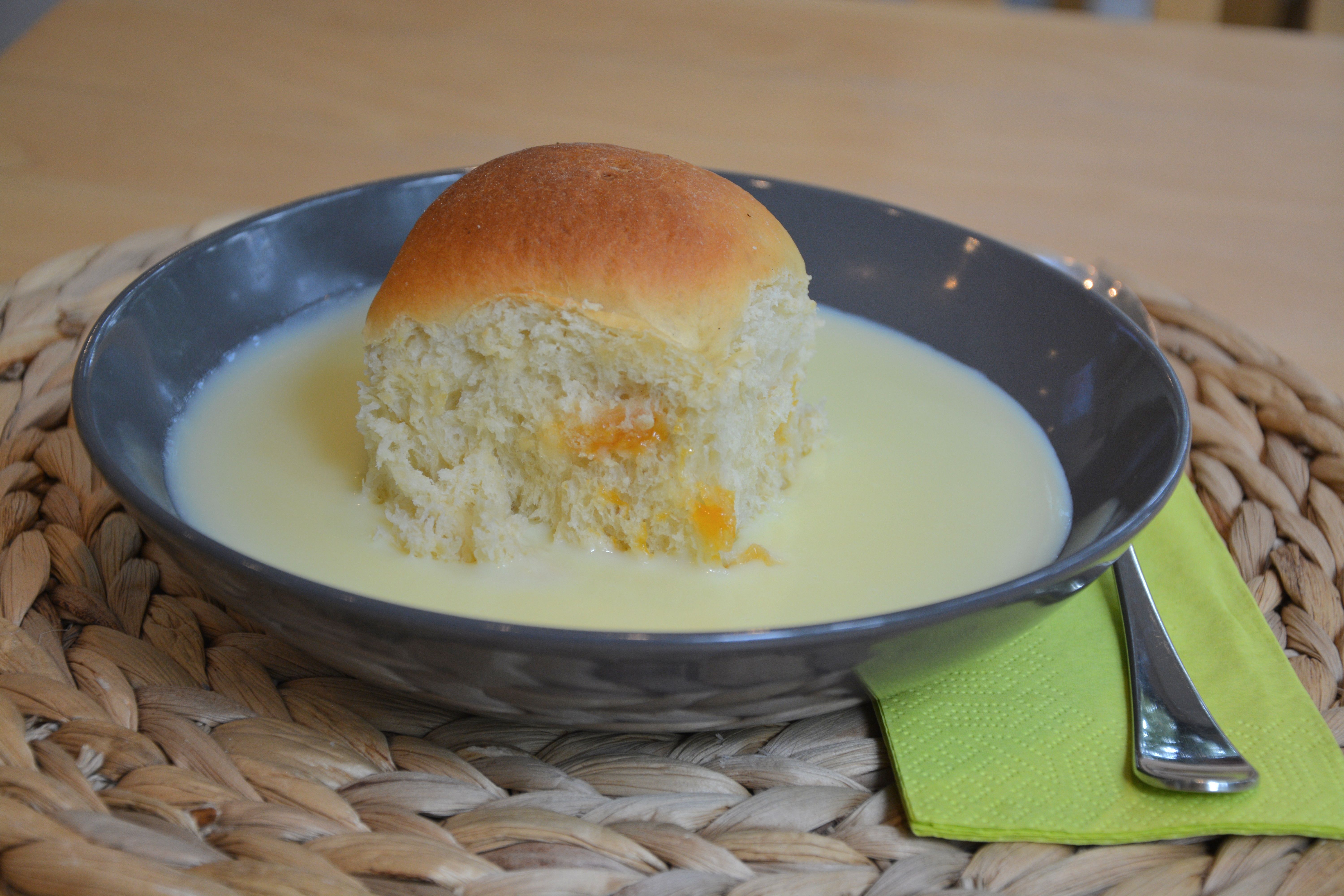 Ein schwarzes Teller mit einer Buchtel und Vanillesoße, daneben grüne Serviette mit Gabel.