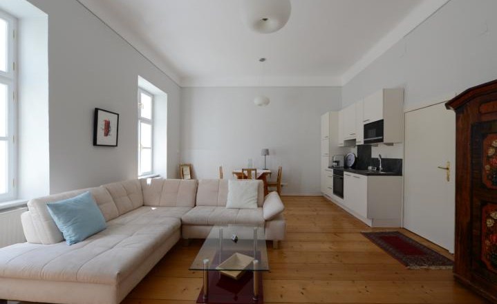 Helles Wohnzimmer mit Ecksofa, Glastisch, Esstisch und Küchenzeile.