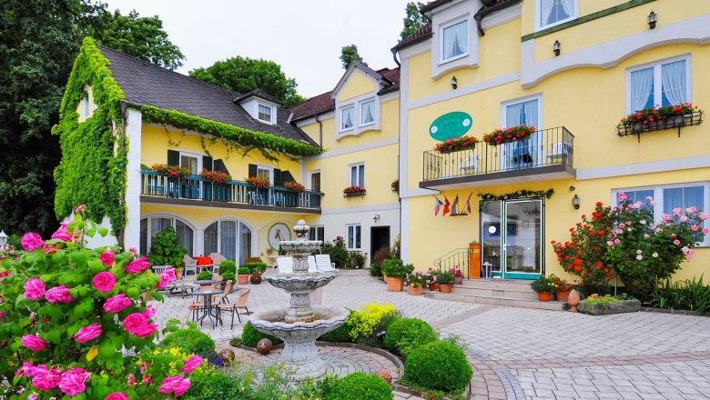 Gelbes Hotelgeb&auml;ude mit Blumenschmuck und Springbrunnen im Vordergrund.