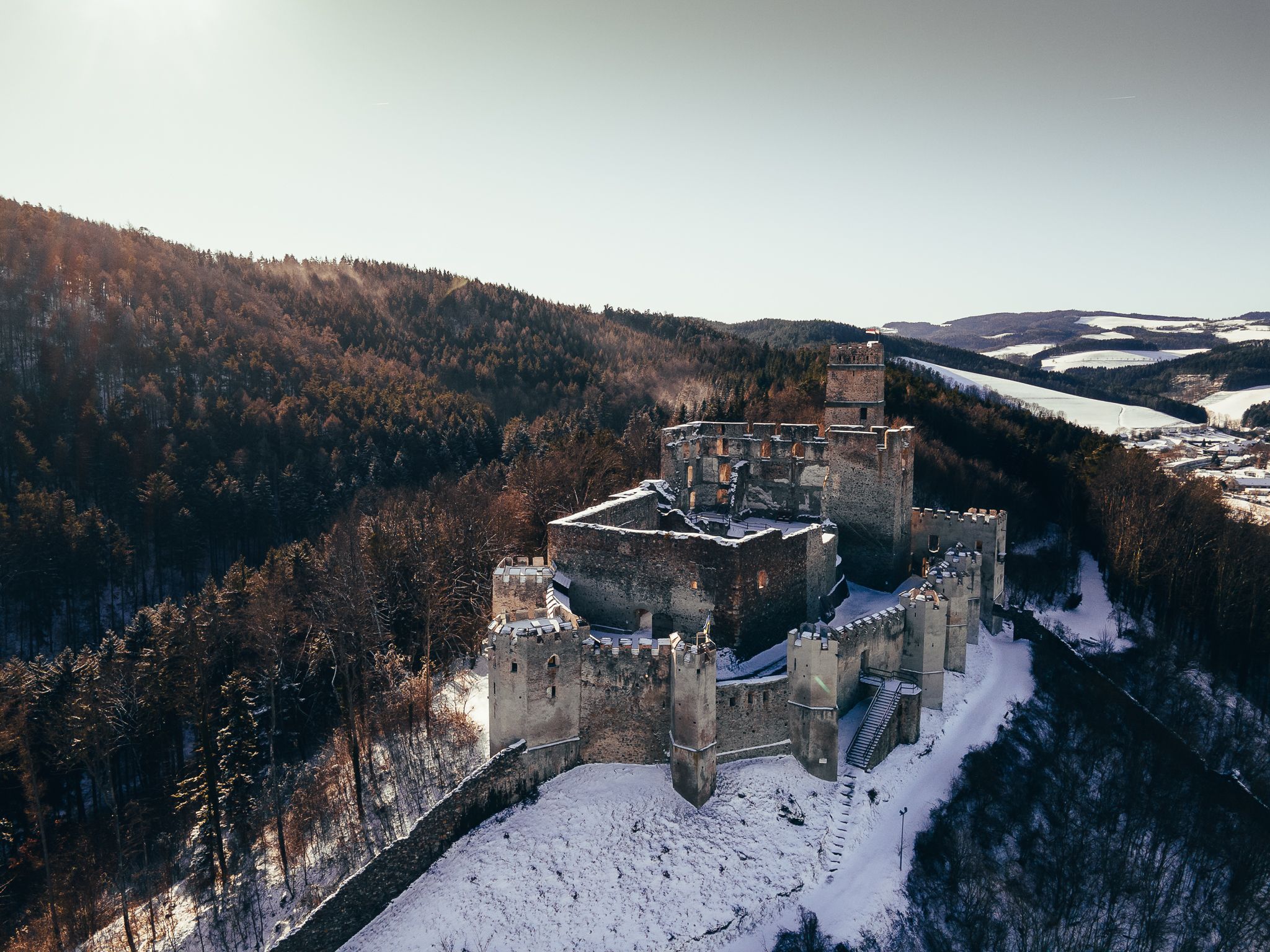 Luftaufnahme der Burgruine Kirchschlag im Winter, umgeben von schneebedeckten Wäldern.