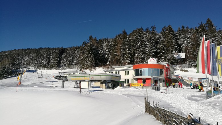 Sesselliftstation in M&ouml;nichkirchen im Winter mit schneebedecktem Gel&auml;nde und Wald im Hintergrund.