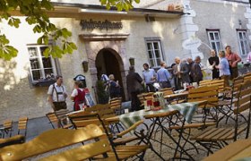 Menschen vor einem traditionellen Gasthaus mit Biergarten.
