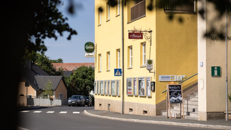 Gelbes Gebäude neben Straße und Zebrastreifen, mit Stufen und s'Hutwisch-Schild.