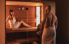 Ein Mann und eine Frau in Handtüchern in einer Sauna.