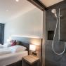 Modernes Hotelzimmer mit Doppelbett und offener Dusche.