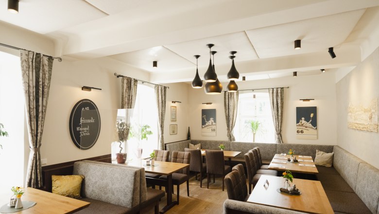 Modernes Restaurant mit Holztischen, grauen Polsterbänken und stilvollen Lampen.