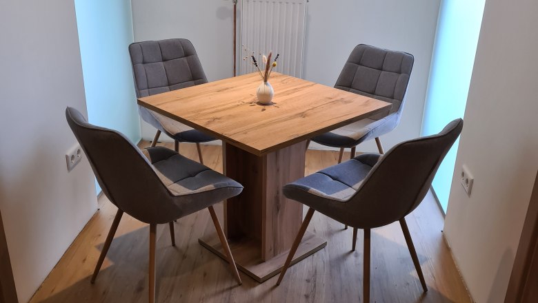 Ein moderner Esstisch mit vier grauen St&uuml;hlen in einem hellen Raum.