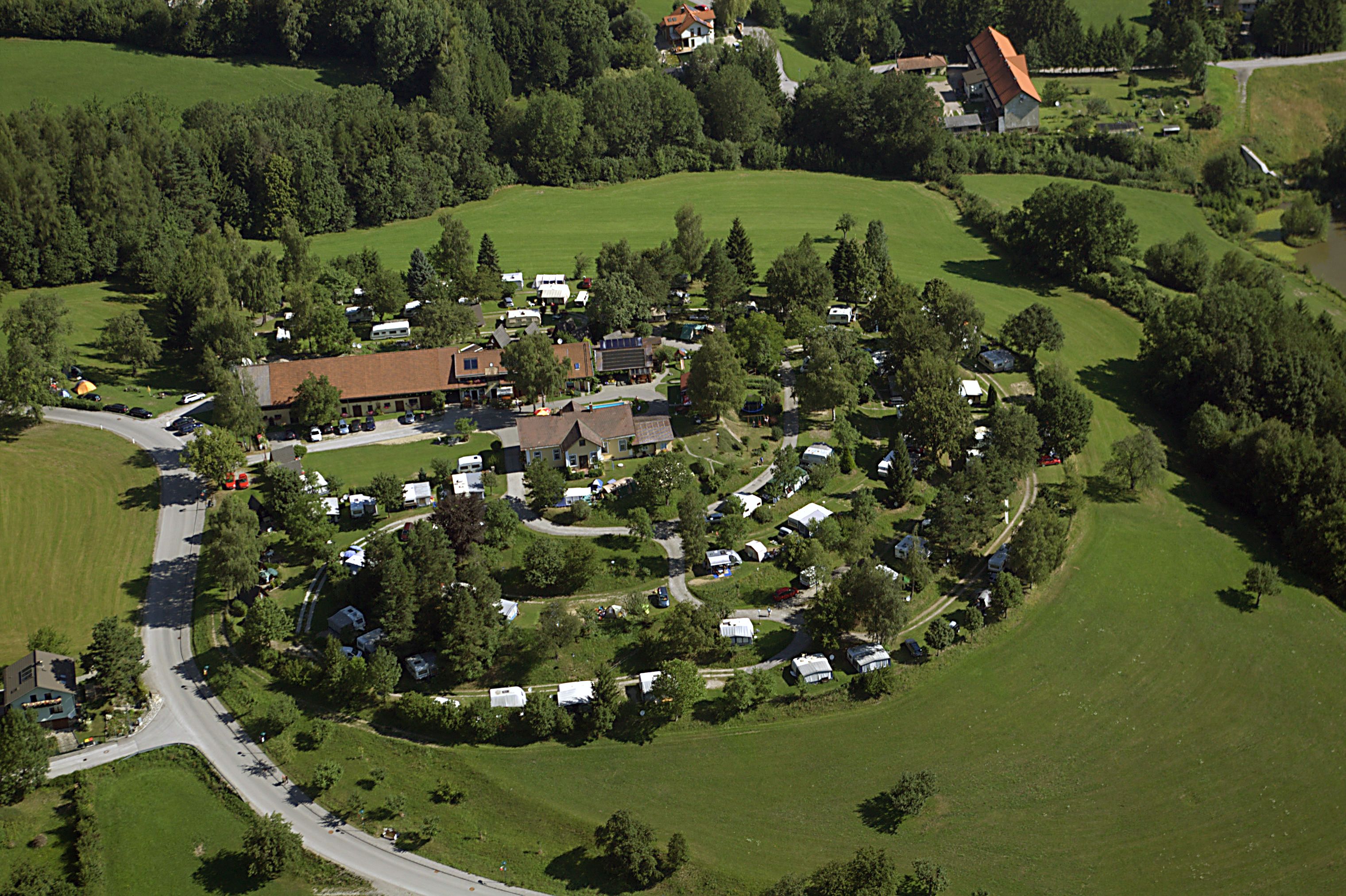 Luftaufnahme eines Campingplatzes inmitten grüner Landschaft mit Wohnwagen und Zelten.