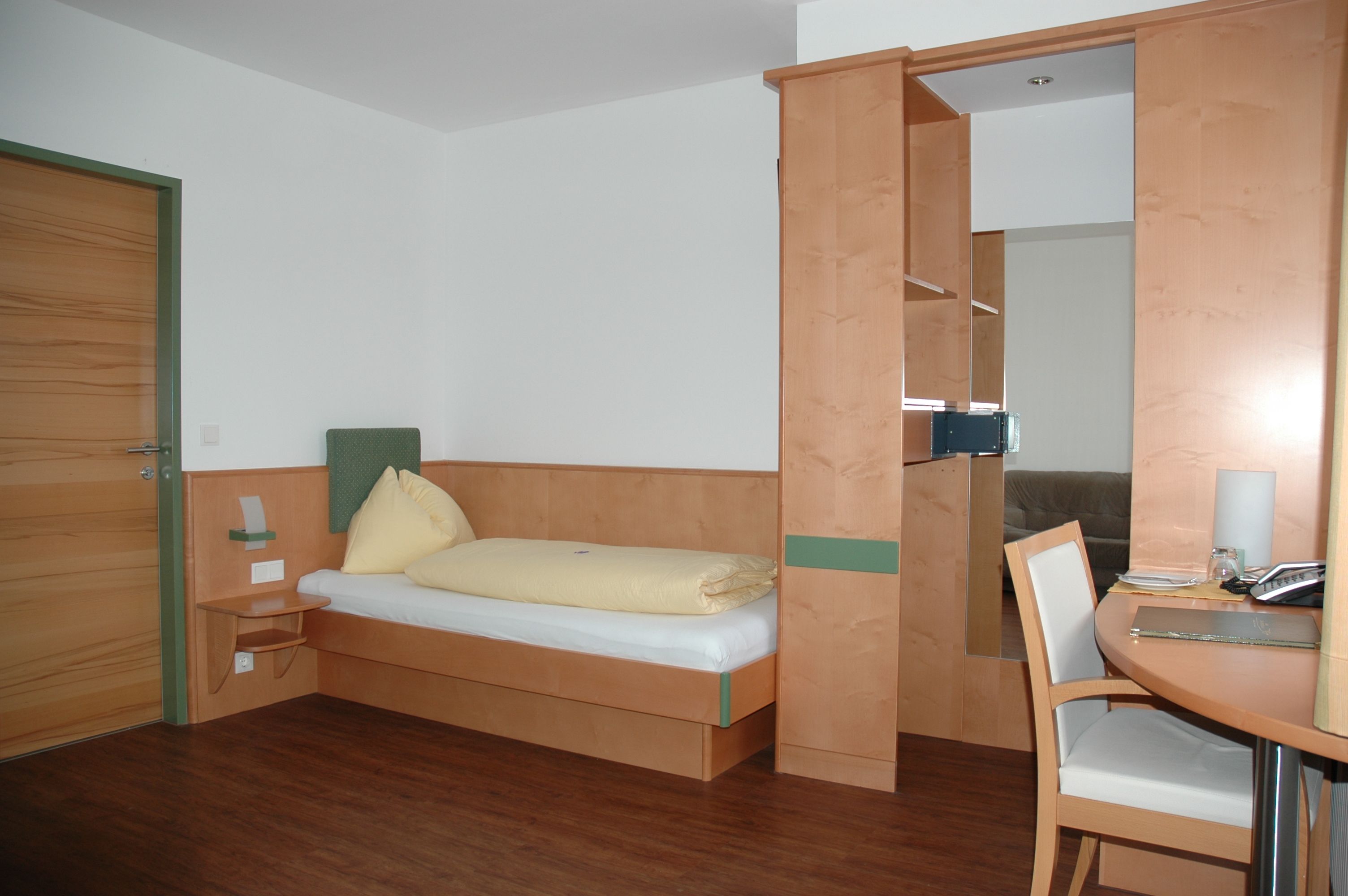 Ein einfach eingerichtetes Hotelzimmer mit Einzelbett, Schreibtisch und Holzverkleidung.