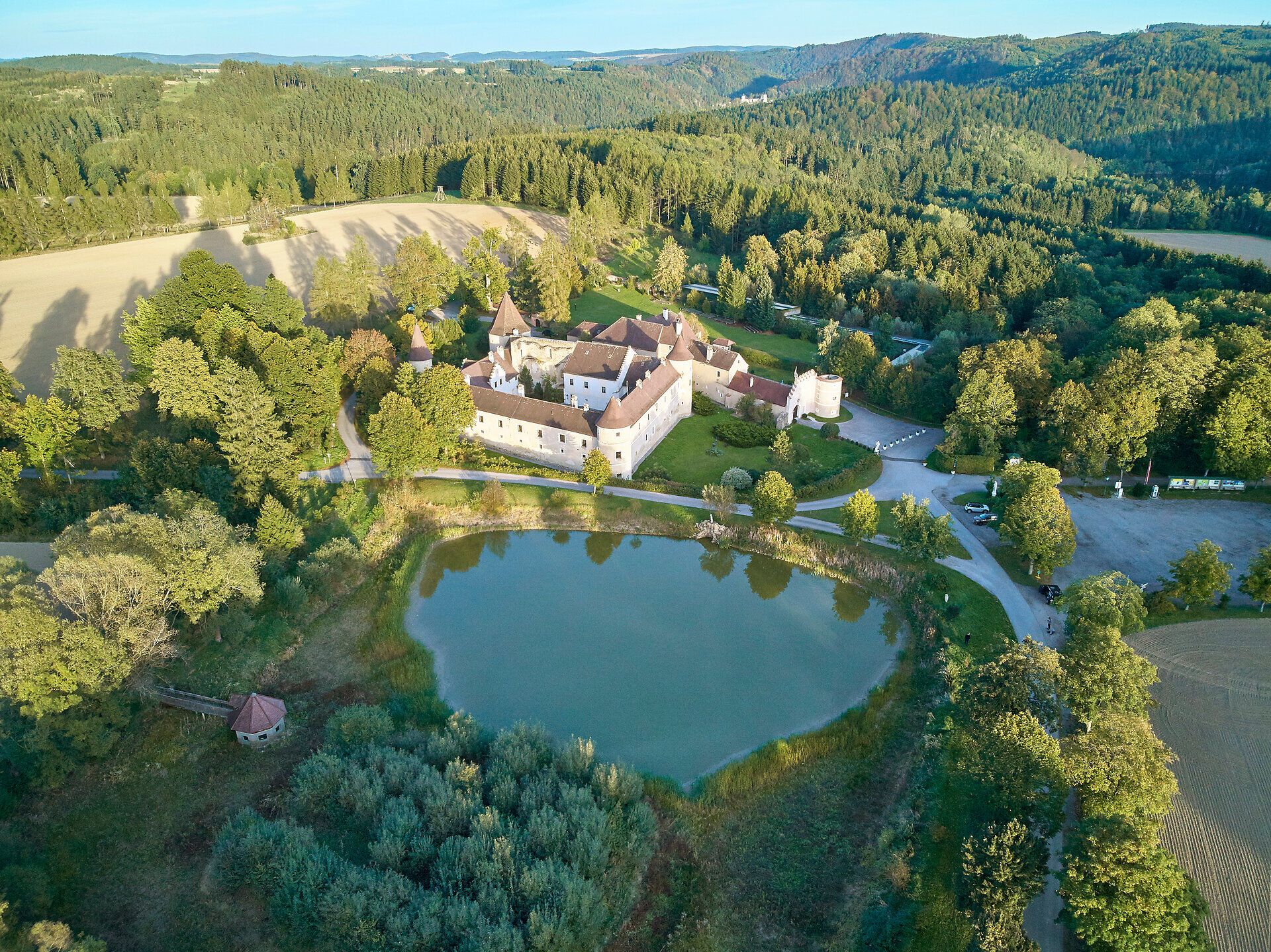 Luftaufnahme von Schloss Waldreichs umgeben von Wald und einem Teich.