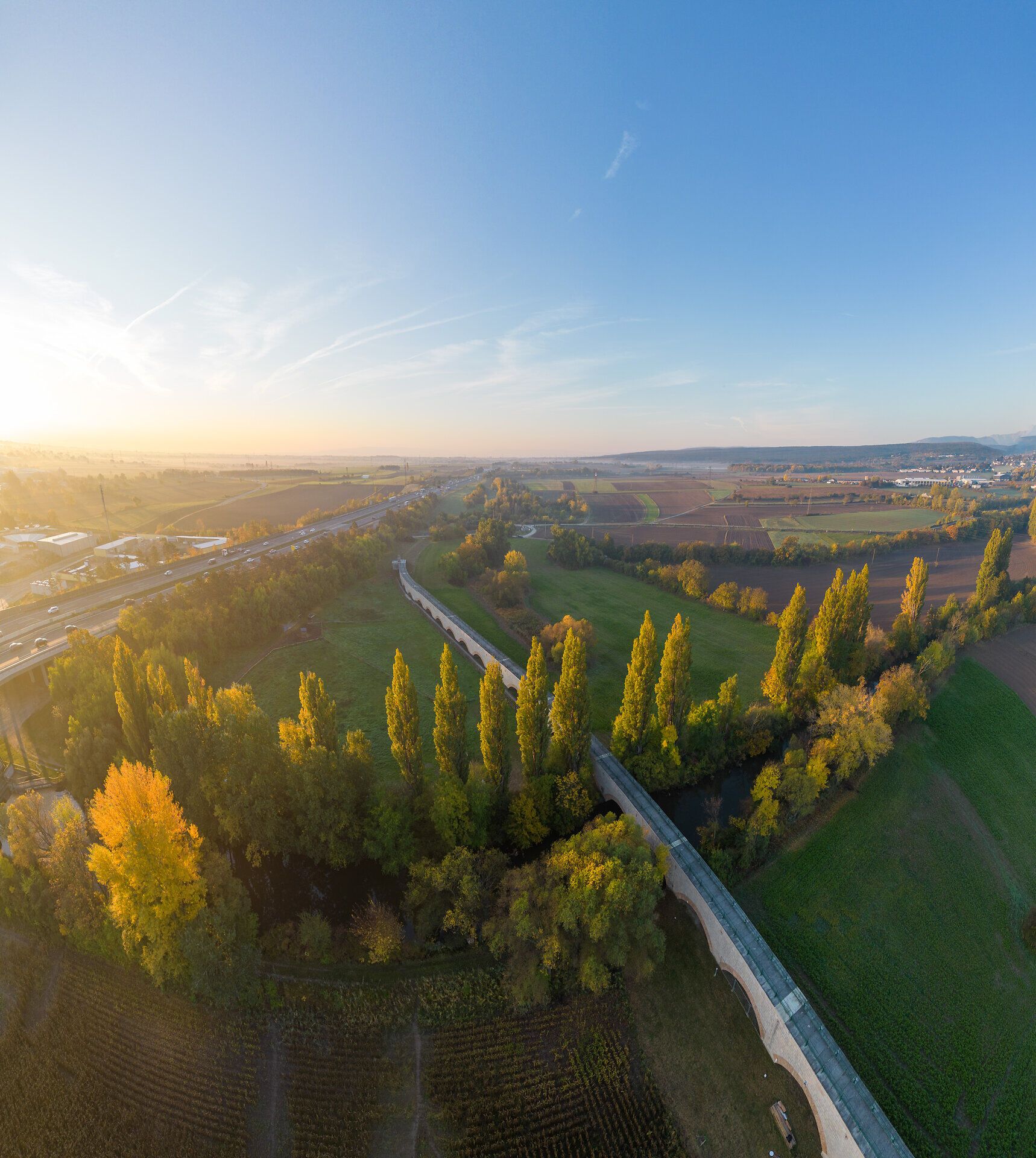 Aquädukt der ersten Wiener Hochquellenleitung bei Leobersdorf im Herbst: langgestreckter Bau mit Rundbögen entlang der Landschaft, umgeben von gelb und orange verfärbten Bäumen.