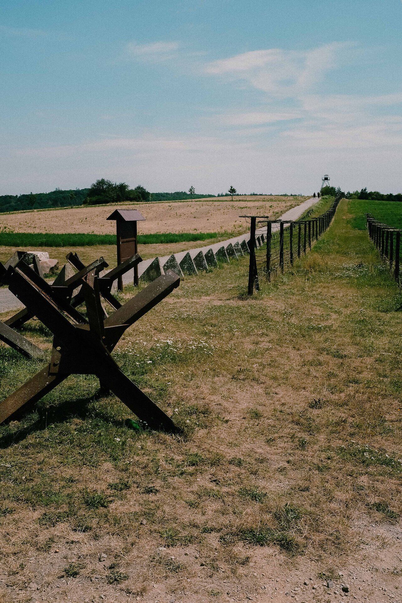 Ein eindrucksvoller Blick auf die weitläufige Landschaft, die von historischen Stacheldrahtverhauen gesäumt ist. Die sanften Hügel und das klare Blau des Himmels schaffen eine Atmosphäre der Ruhe und Besinnung, während die Natur ihre Schönheit entfaltet.