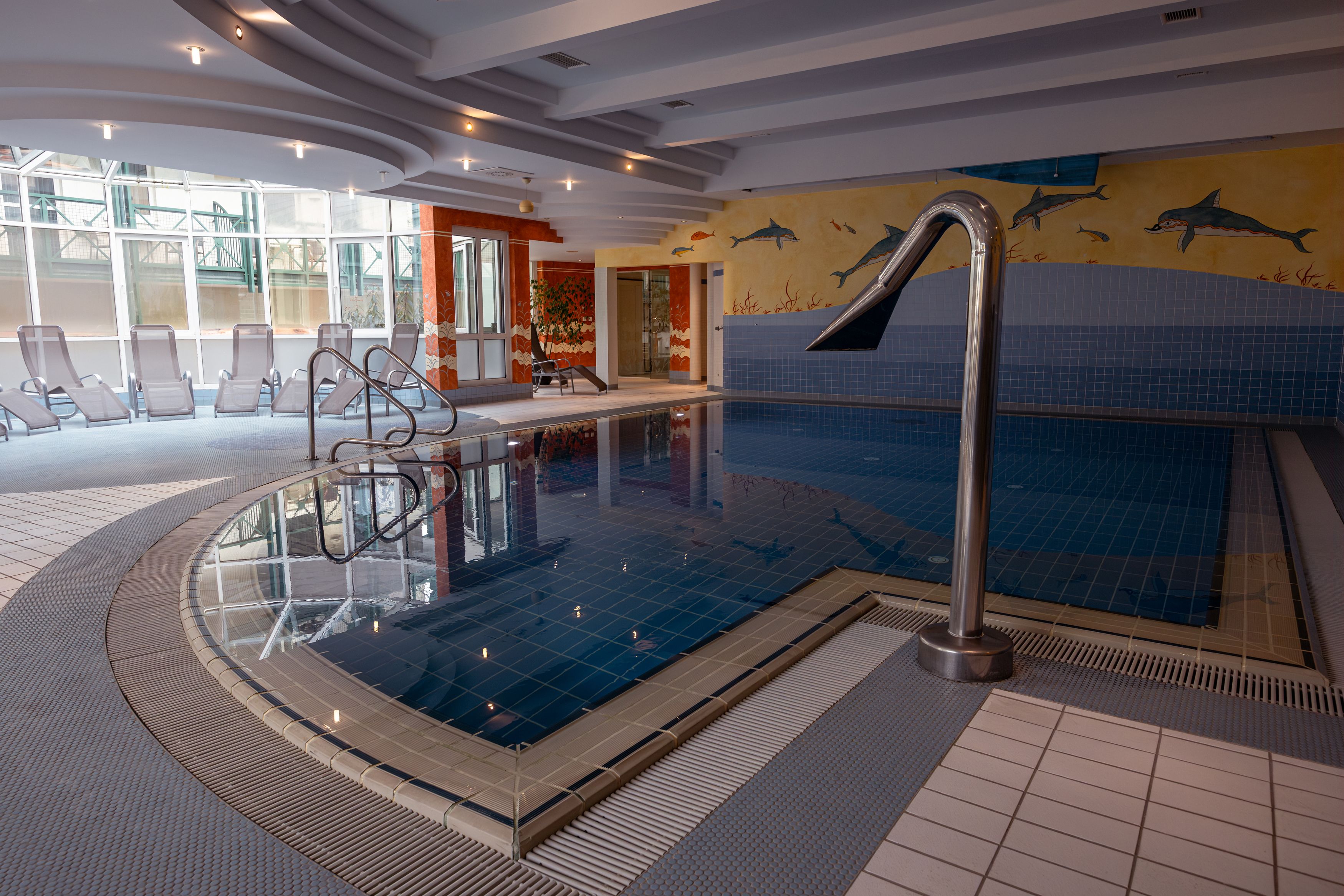 Innenansicht eines Hotelpools mit Liegestühlen und Wandmalerei von Delfinen.