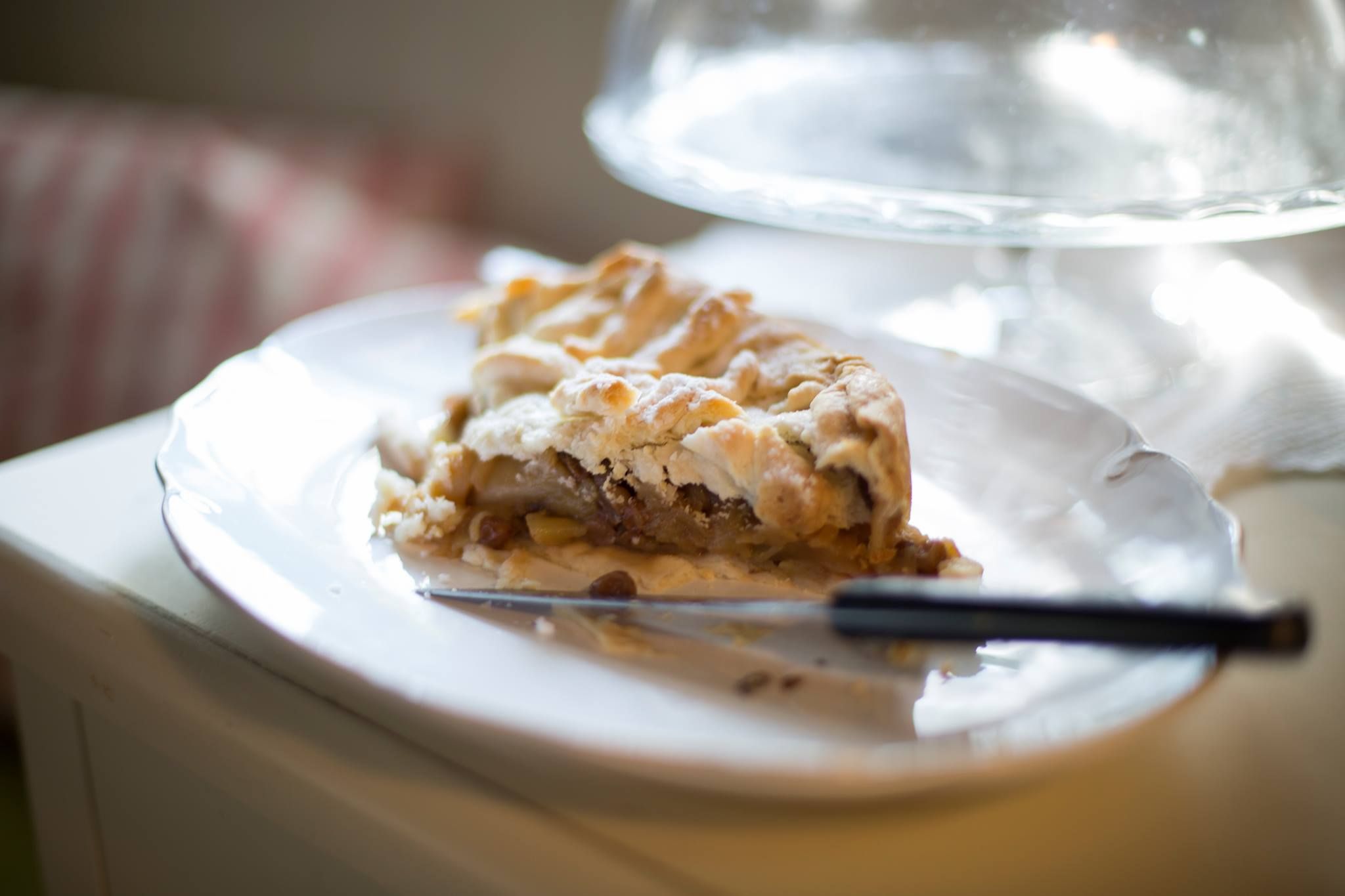 Ein Stück Apfelkuchen auf einem weißen Teller mit einem Messer daneben.