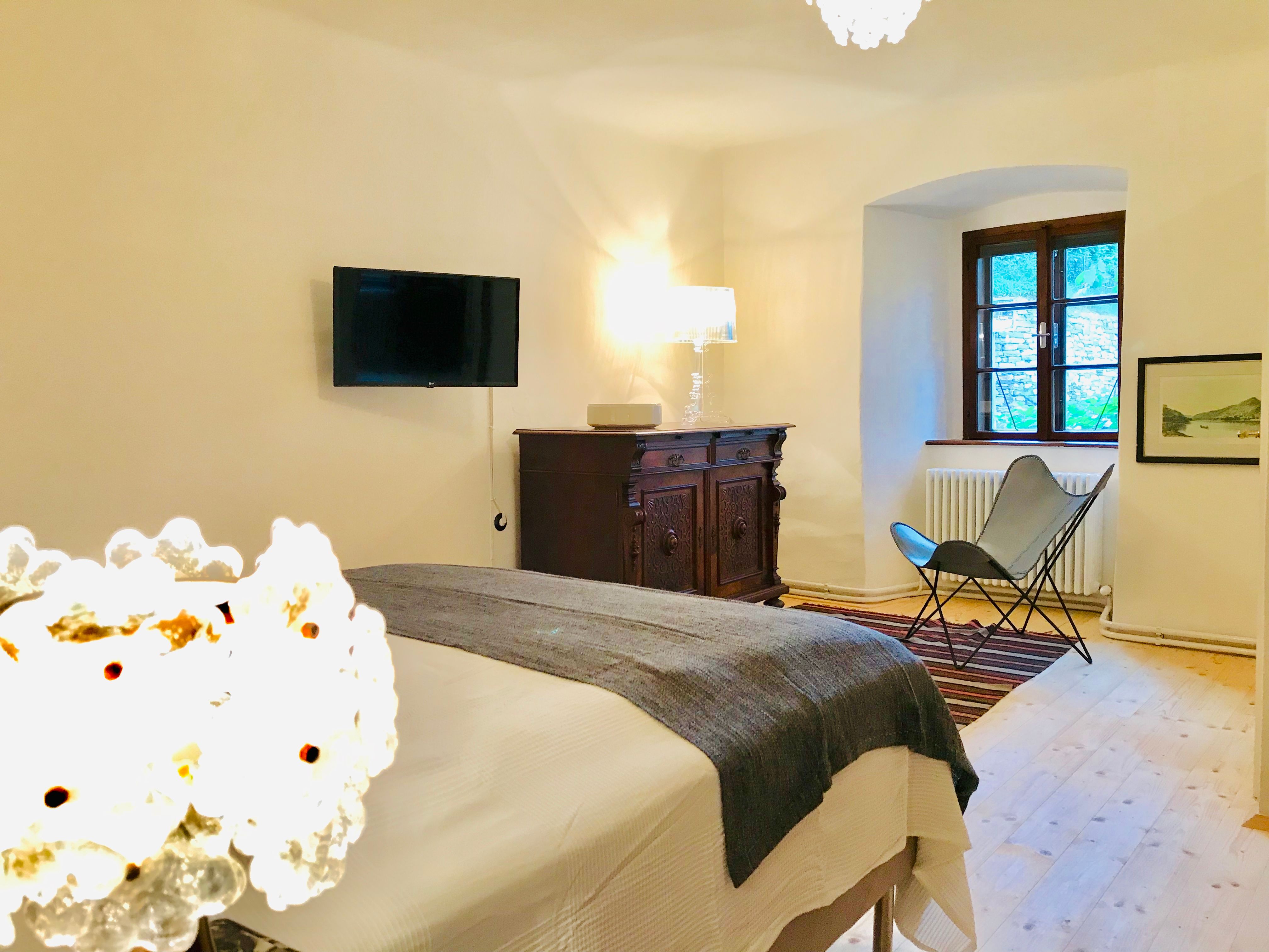 Gemütliches Schlafzimmer mit Bett, antiker Kommode, Sessel und Wand-TV.