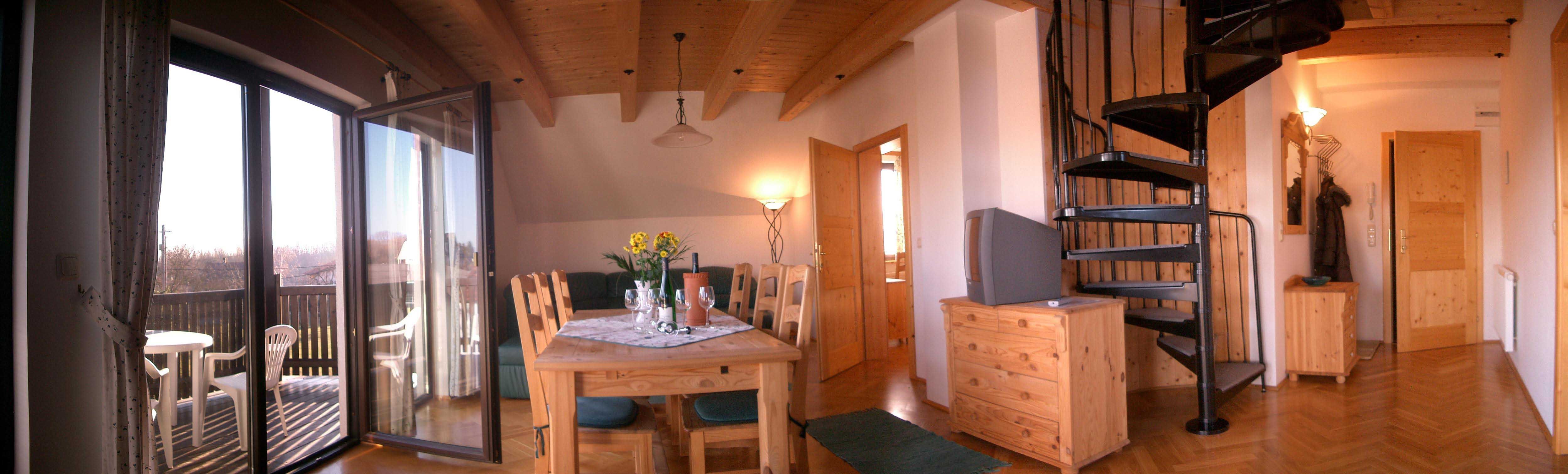Wohnzimmer mit Holzmöbeln, Esstisch, Wendeltreppe und Balkon.