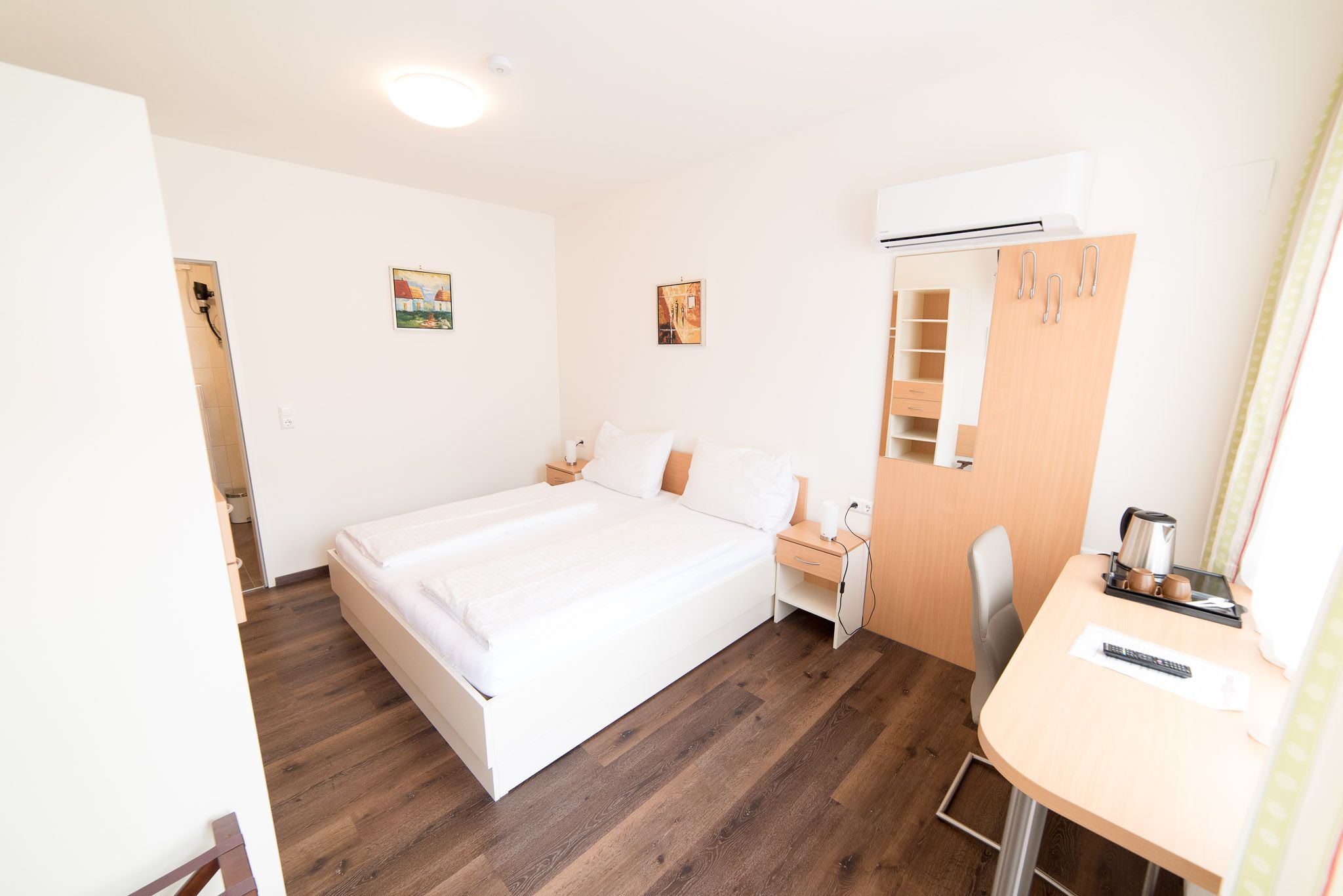 Helles Schlafzimmer mit Schrank, Doppelbett, Nachtkästchen, Schreibtisch.