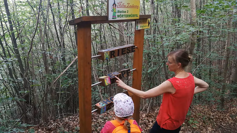 Zwei Personen an einer Station im Wald mit Wortwürfeln auf Millas Zauberweg.