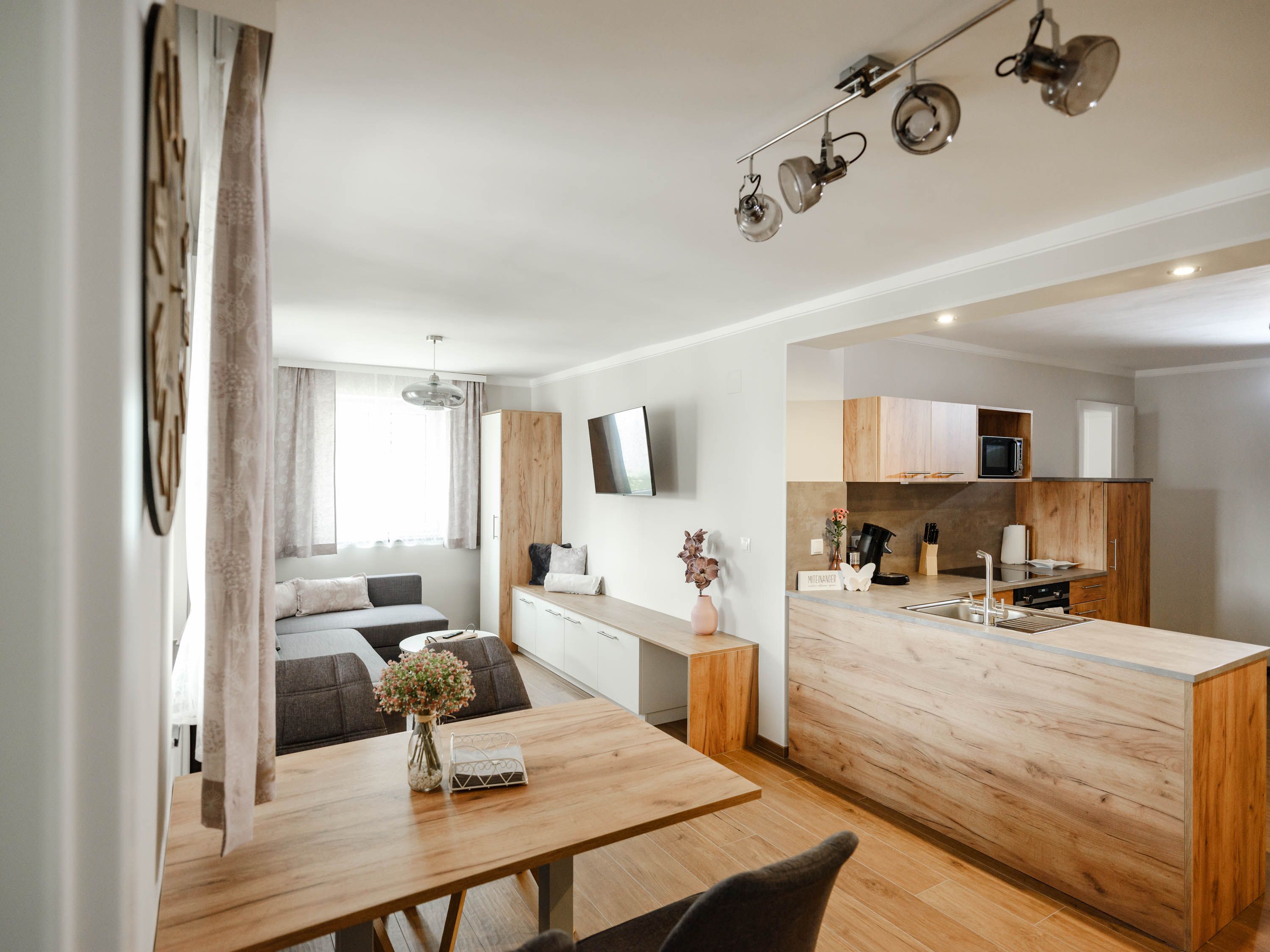 Moderne Wohnküche mit Holzmöbeln und grauem Sofa.