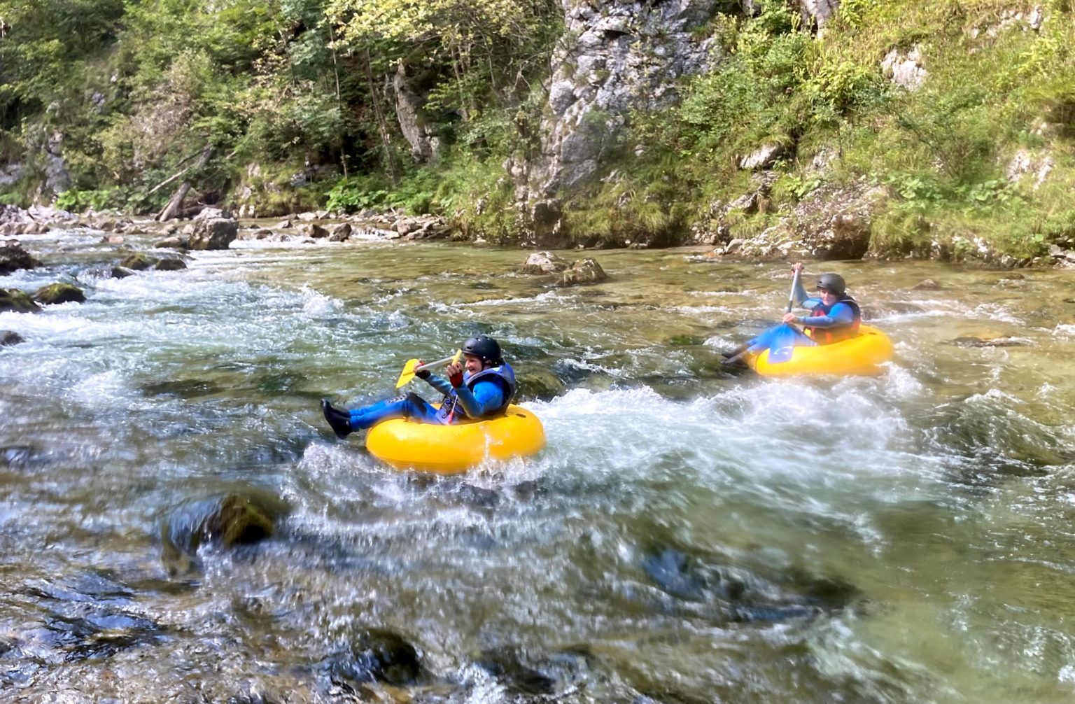 Zwei Personen beim Tubing auf einem Fluss in einer bewaldeten Umgebung.