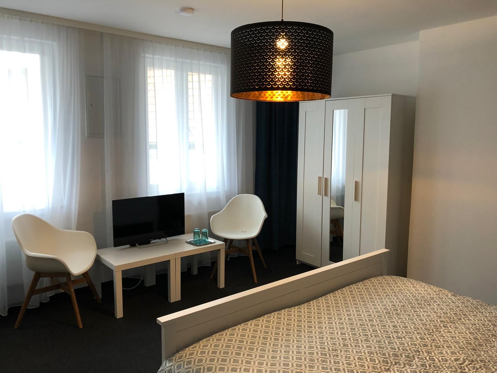 Modern eingerichtetes Doppelzimmer mit Bett, Schrank, zwei Stühlen, kleinem Tisch und Fernseher.