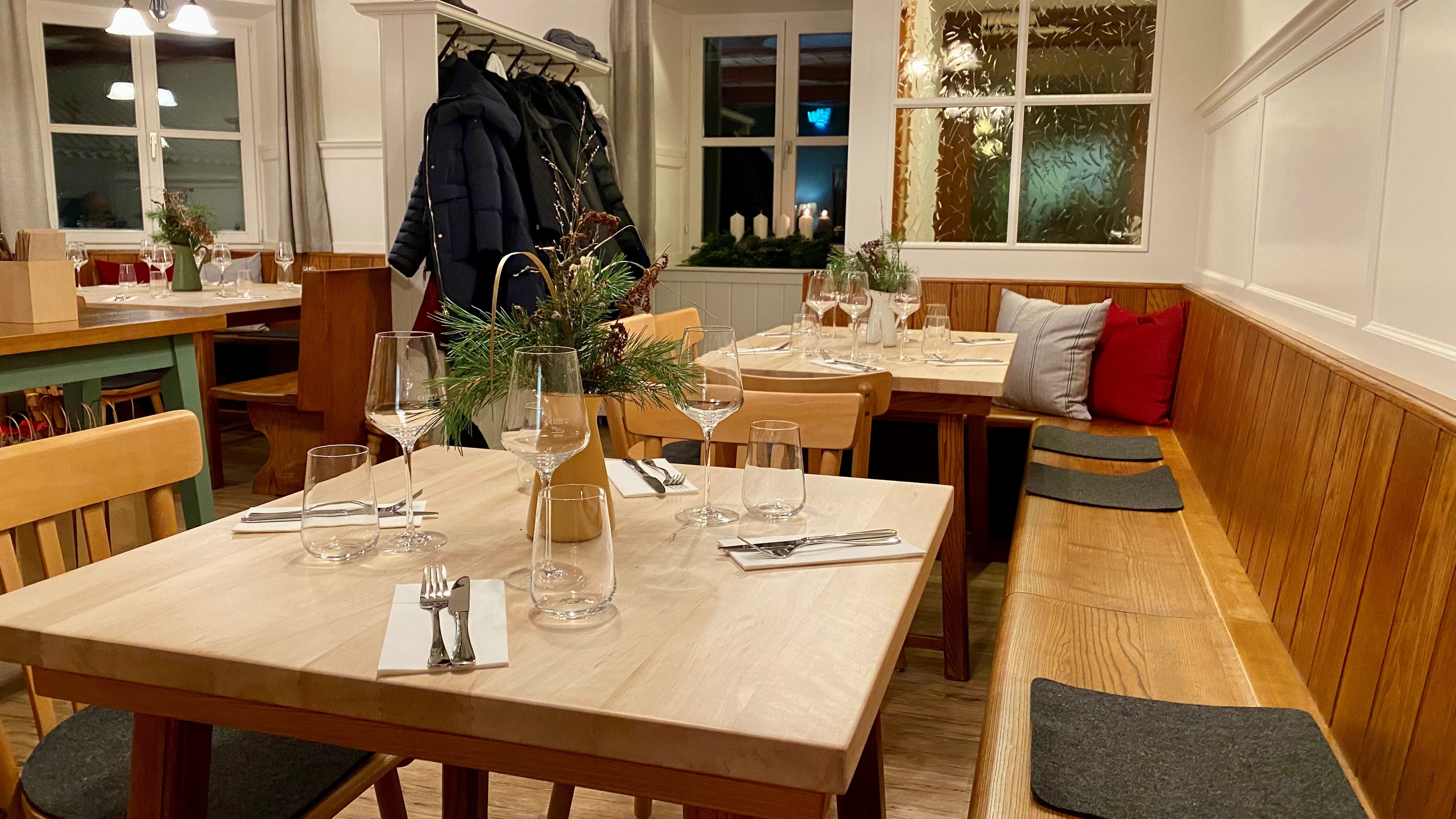 Die Gaststube mit Holzbank, Holztischen und Garderobe.